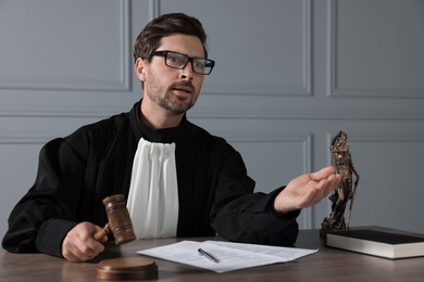 Photo of Judge with gavel, papers and book sitting at wooden table indoors