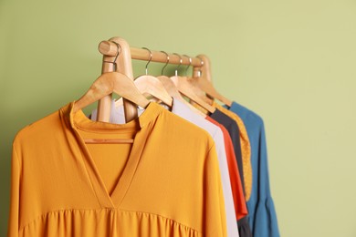 Photo of Collection of trendy women's garments on rack near green wall, closeup. Clothing rental service