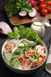 Photo of Bowl of delicious vegetable salad dressed with mayonnaise and ingredients on black table