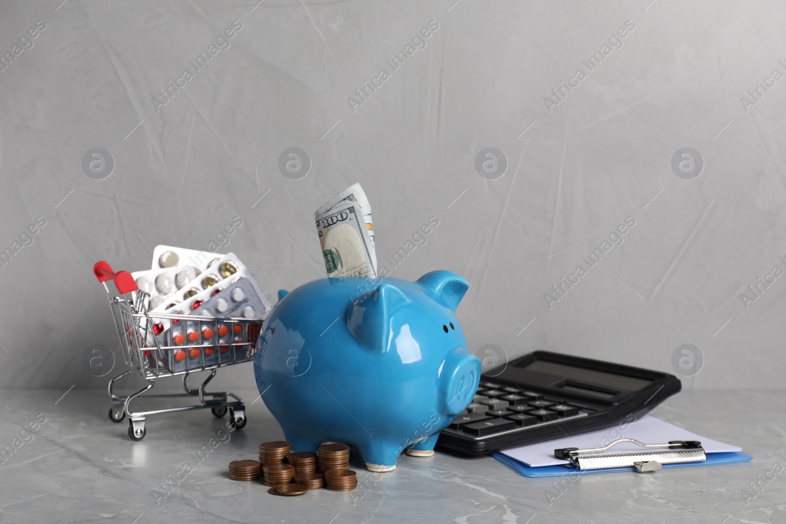 Photo of Piggy bank with money, calculator, clipboard and pills on light grey table. Medical insurance