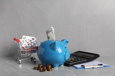 Photo of Piggy bank with money, calculator, clipboard and pills on light grey table. Medical insurance