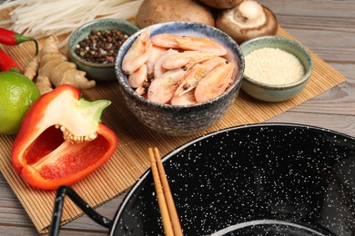 Photo of Black wok, chopsticks and bamboo mat with products on color wooden table, closeup
