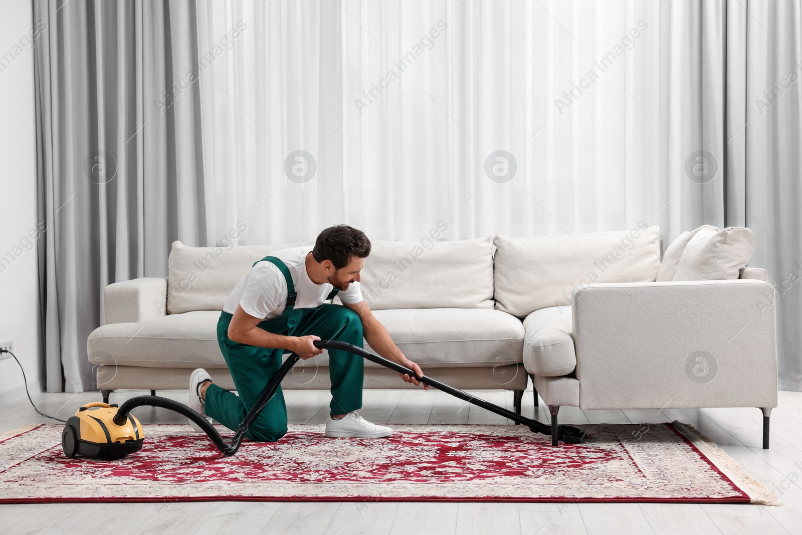 Photo of Dry cleaner's employee hoovering carpet with vacuum cleaner in room