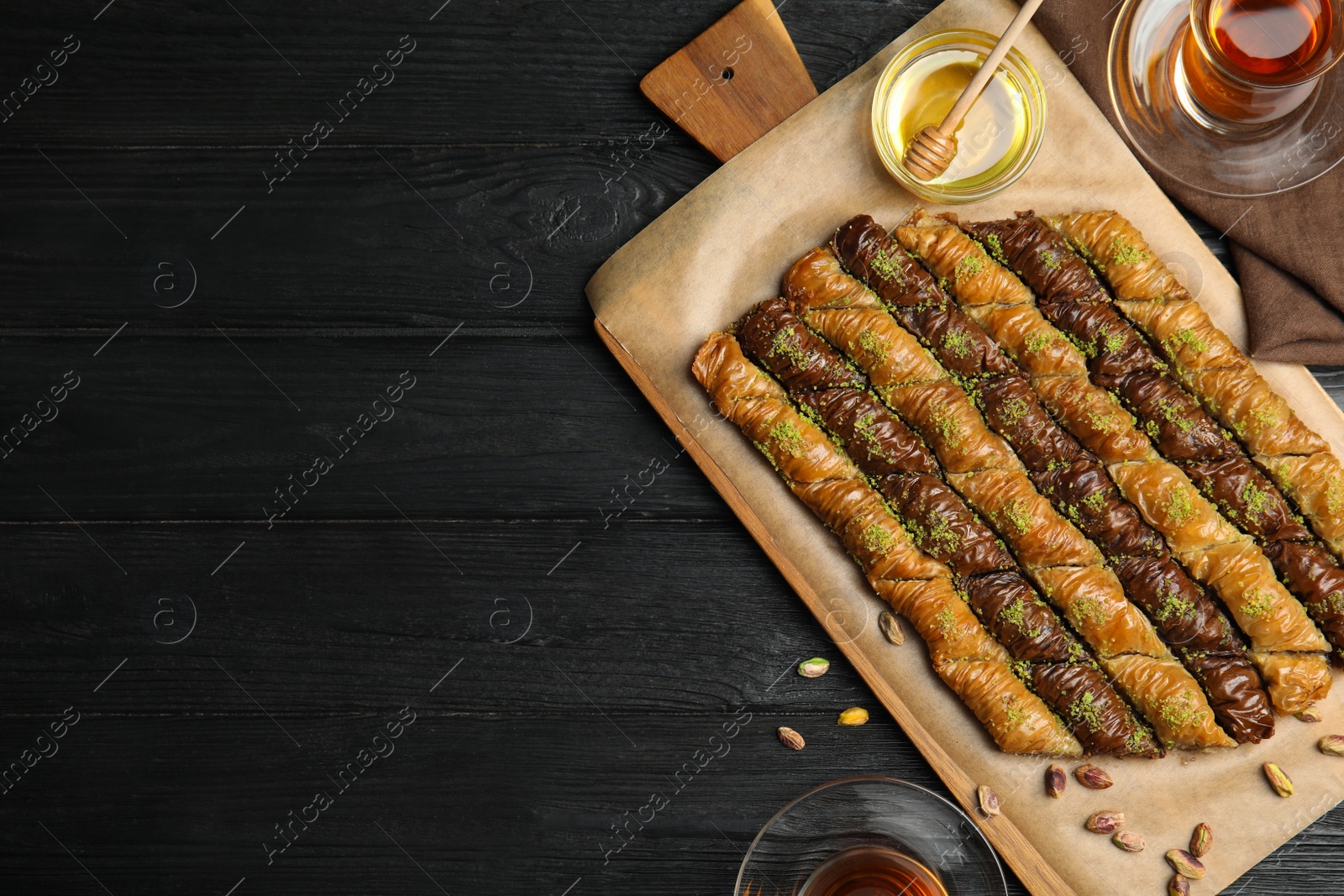 Photo of Delicious sweet baklava with honey and hot tea on black wooden table, flat lay. Space for text