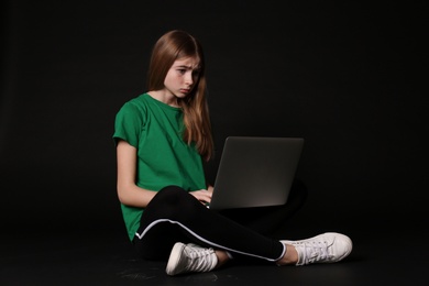 Shocked teenage girl with laptop on black background. Danger of internet