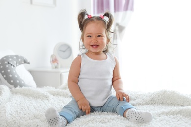 Adorable little baby girl sitting on bed in room