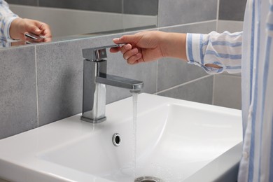Woman opening water tap in bathroom, closeup