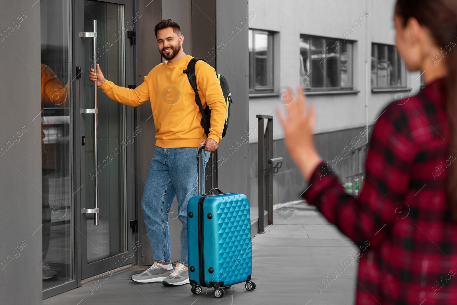 Photo of Long-distance relationship. Woman waving to her boyfriend with luggage near building outdoors, selective focus