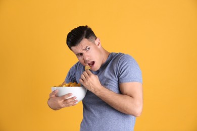 Photo of Greedy man hiding bowl with chips on yellow background