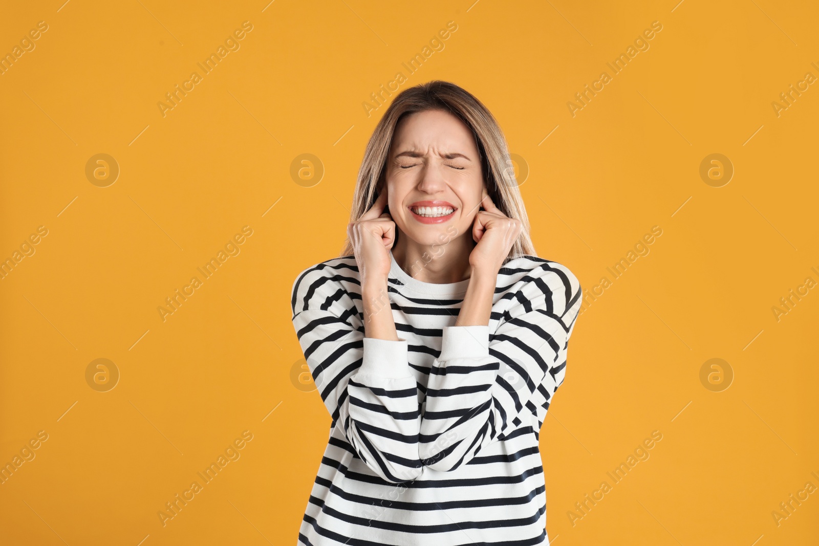 Photo of Emotional young woman covering her ears with fingers on yellow background