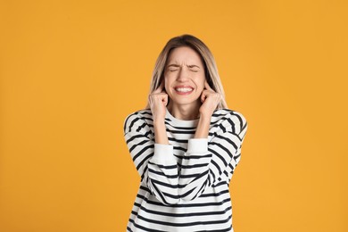 Emotional young woman covering her ears with fingers on yellow background