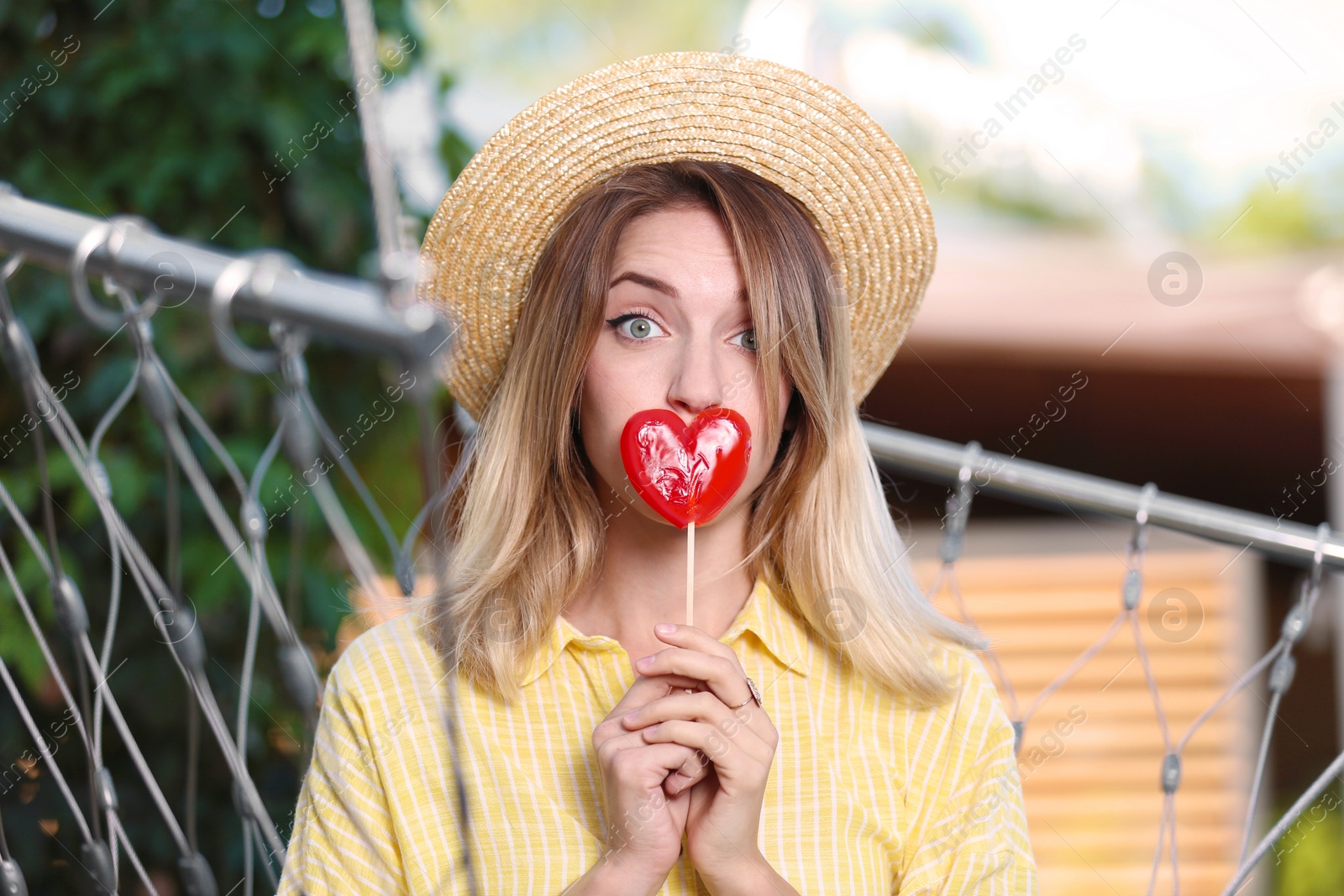 Photo of Young woman with candy relaxing in hammock chair outdoors