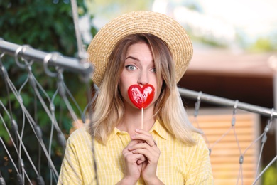 Photo of Young woman with candy relaxing in hammock chair outdoors