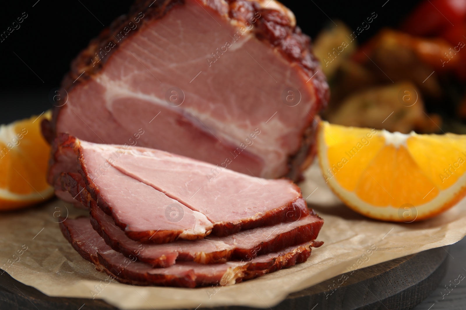 Photo of Cut delicious ham and orange on parchment paper, closeup