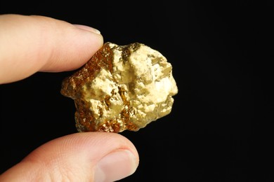 Woman holding gold nugget against black background, closeup. Space for text