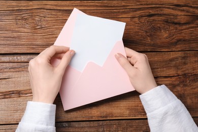 Woman taking card out of letter envelope at wooden table, top view