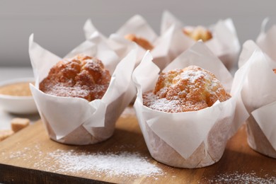 Photo of Delicious muffins with powdered sugar on wooden board, closeup