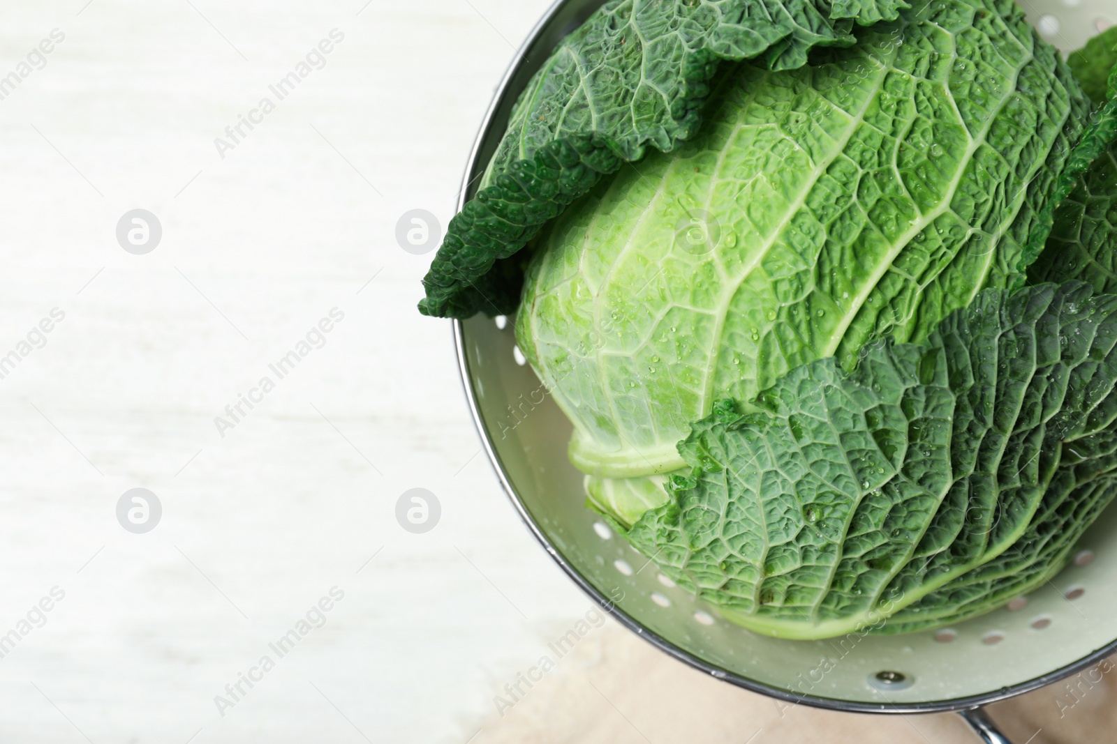 Photo of Colander with savoy cabbage and space for text on white wooden background, top view