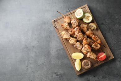 Delicious shish kebabs with vegetables and lemon on grey table, top view. Space for text