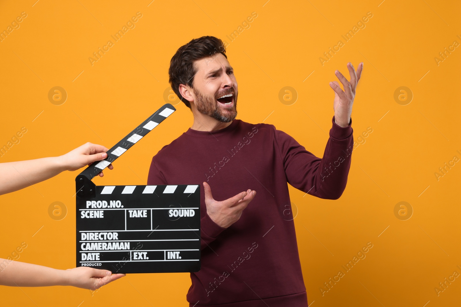 Photo of Emotional actor performing while second assistant camera holding clapperboard on orange background