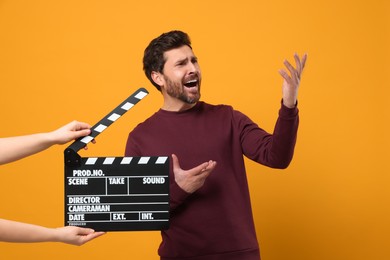 Photo of Emotional actor performing while second assistant camera holding clapperboard on orange background