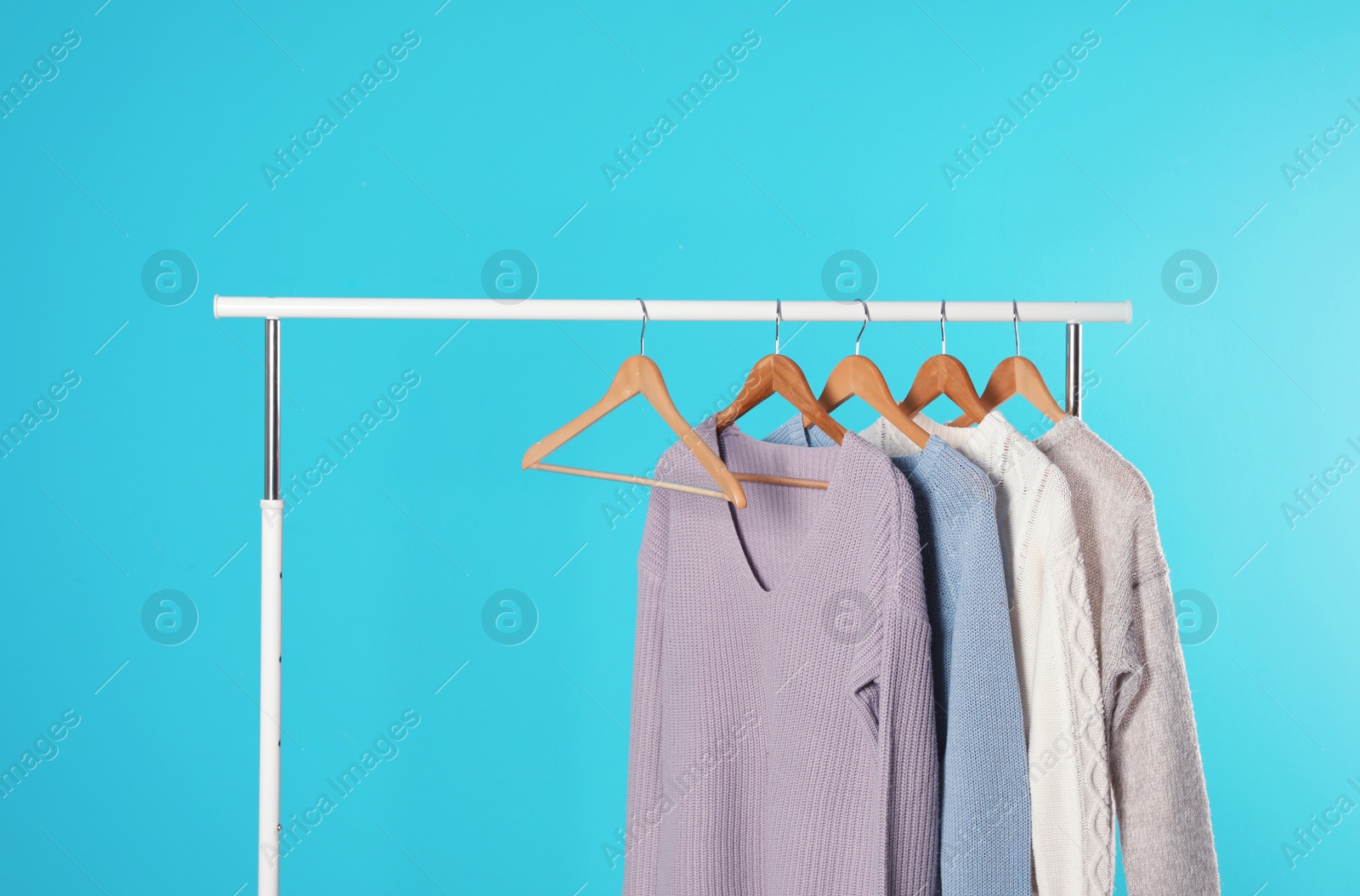 Photo of Collection of warm sweaters hanging on rack against color background