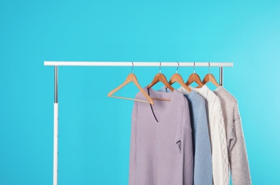 Collection of warm sweaters hanging on rack against color background