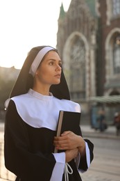 Young nun with Bible near cathedral outdoors on sunny day
