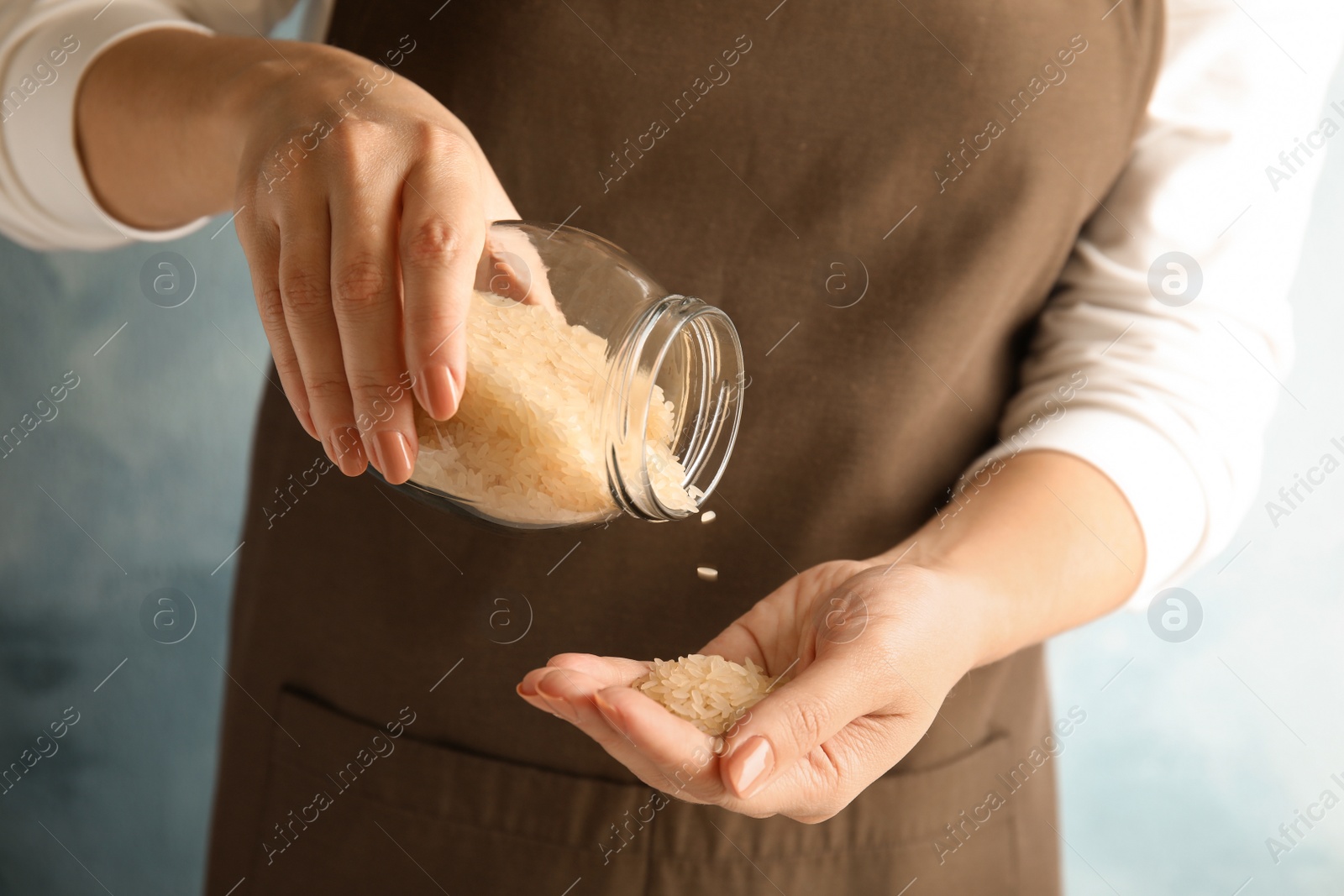 Photo of Woman pouring uncooked rice from jar into hand on color background, closeup