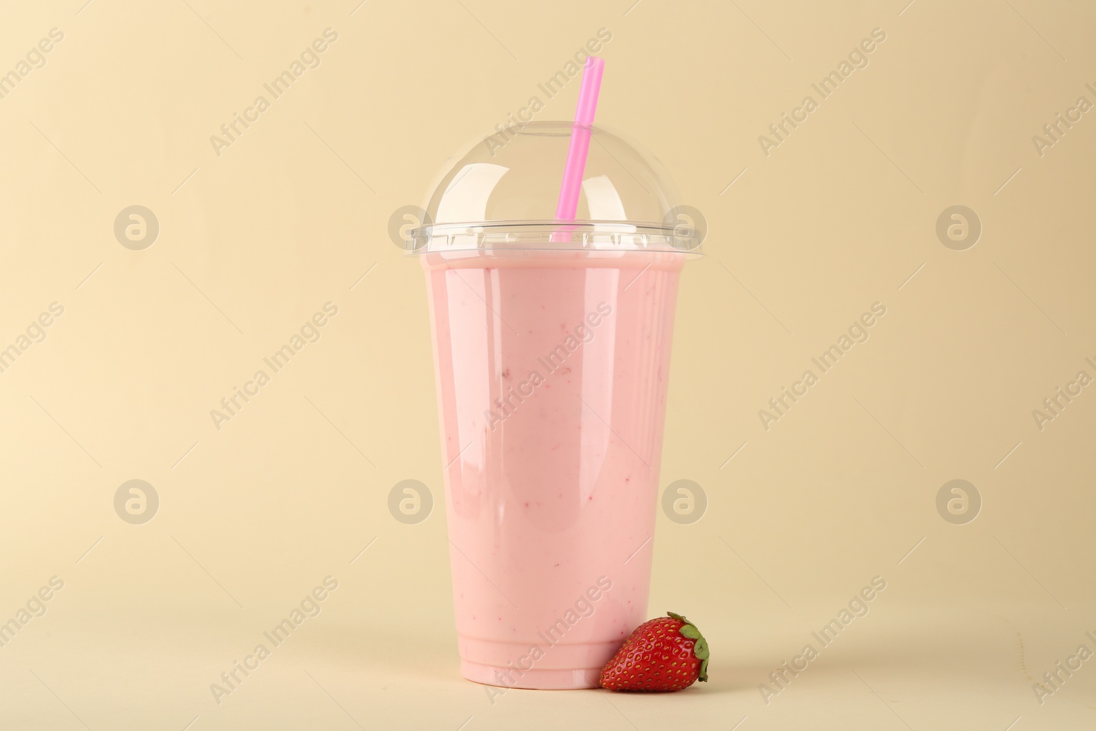 Photo of Plastic cup of tasty smoothie and fresh strawberry on beige background