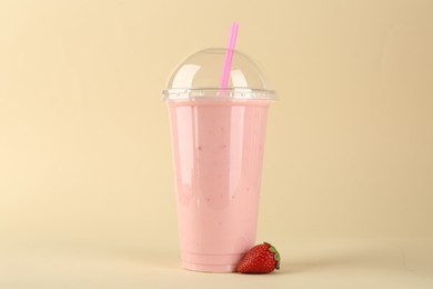 Photo of Plastic cup of tasty smoothie and fresh strawberry on beige background