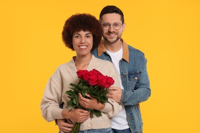 Photo of International dating. Happy couple with bouquet of roses on orange background
