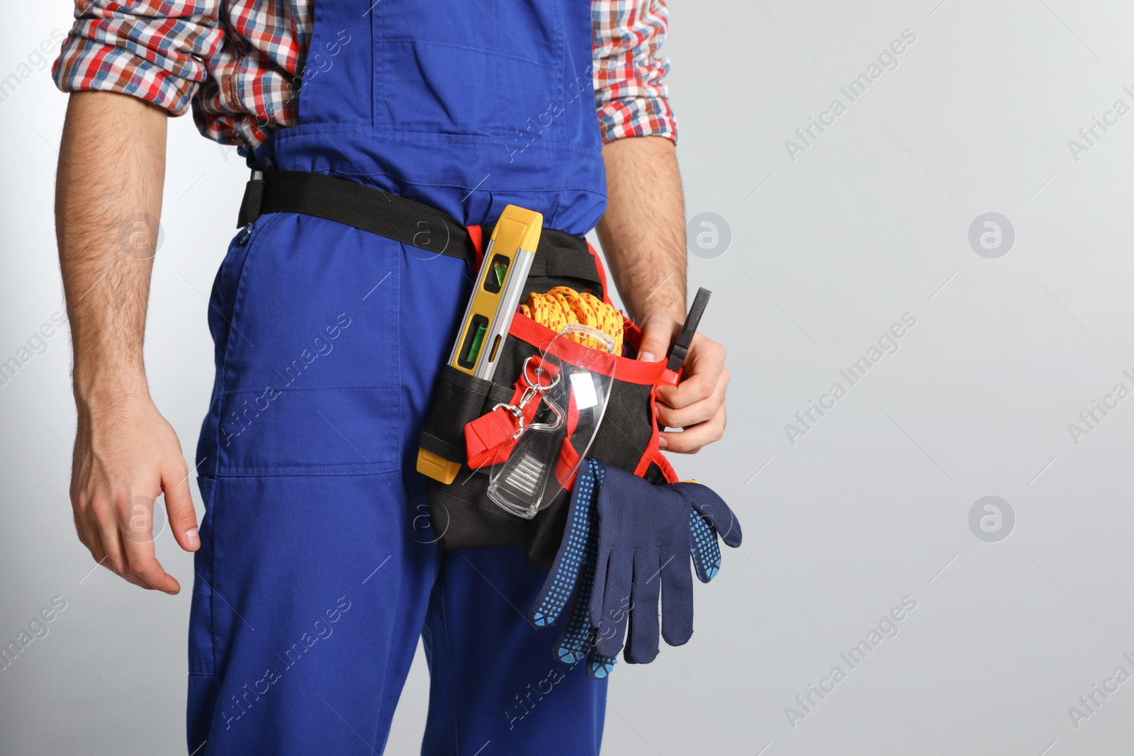 Photo of Construction worker with tool belt on light background, closeup. Space for text