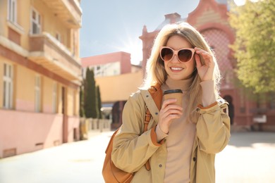 Happy young woman with coffee on city street in morning