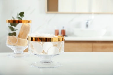 Photo of Jars with cotton pads and loofah sponges on table in bathroom