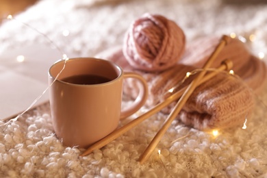 Photo of Composition with cup of hot beverage and knitting yarn on fuzzy rug. Winter evening