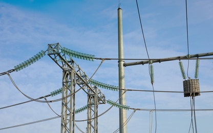 Photo of Electricity transmission power lines against blue sky, closeup view