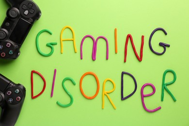 Photo of Phrase Gaming Disorder made of colorful plasticine and gamepads on light green background, flat lay. Addictive behavior