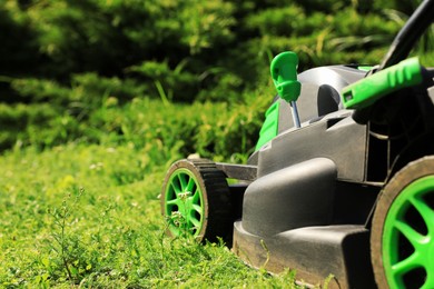 Lawn mower on green grass in garden, closeup. Space for text