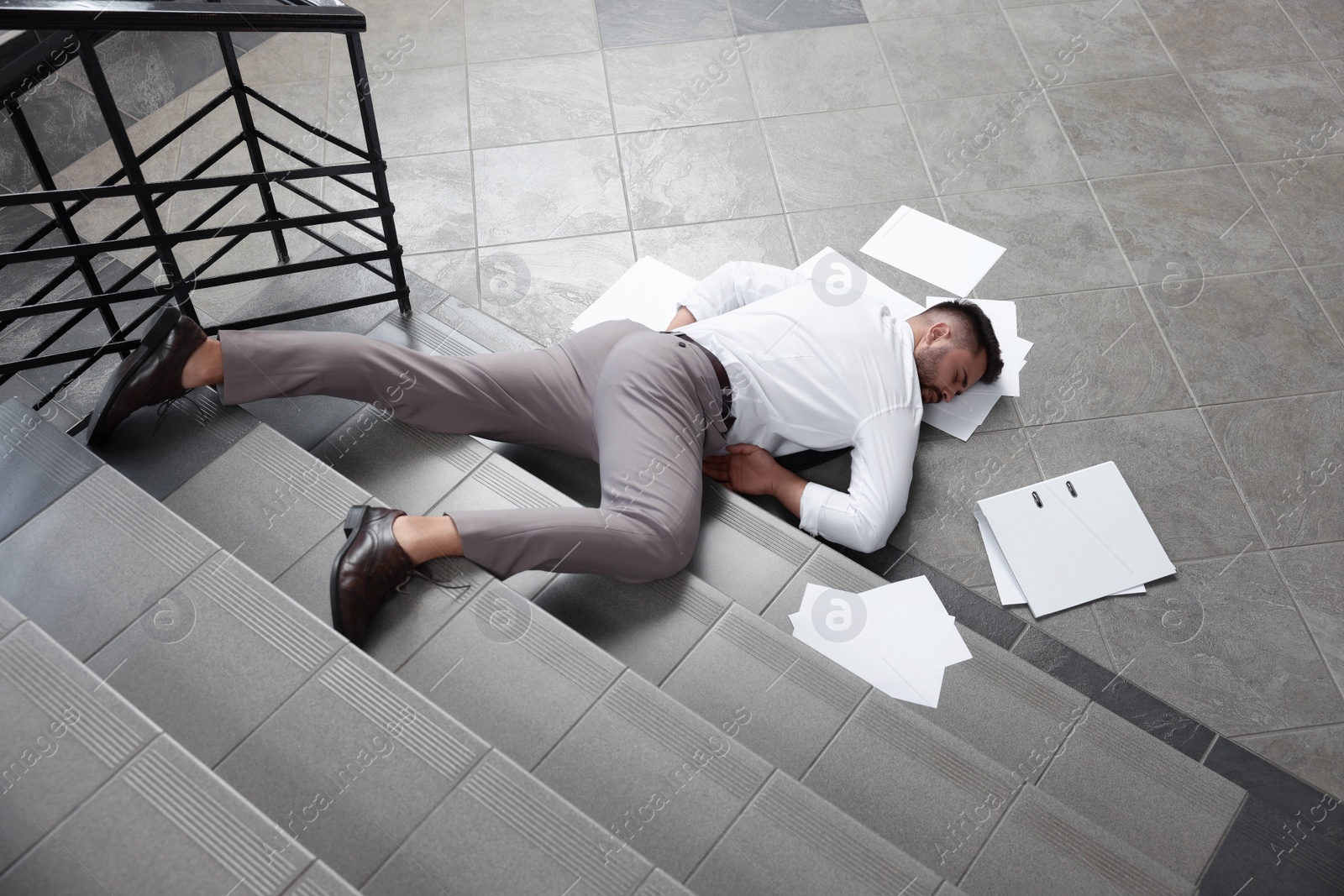 Photo of Unconscious man with scattered folder and papers lying on floor after falling down stairs indoors