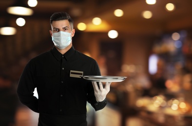 Image of Waiter in medical face mask holding tray in restaurant