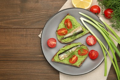 Photo of Delicious sandwiches with sprats, tomatoes, avocado puree and dill on wooden table, flat lay. Space for text