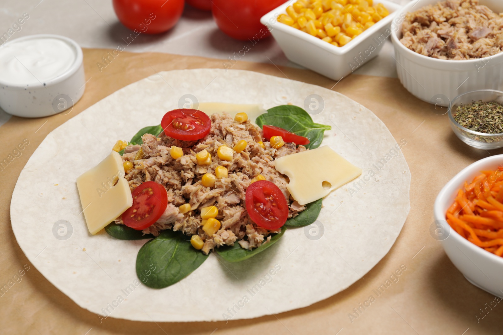 Photo of Delicious tortilla with tuna, vegetables and cheese on light table. Cooking shawarma