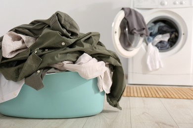 Laundry basket with clothes on floor near washing machine indoors