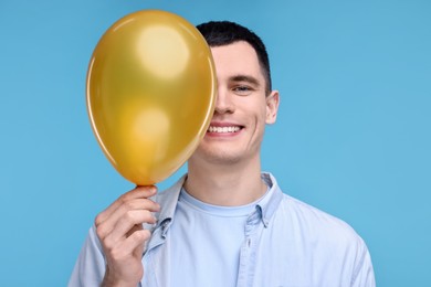 Photo of Happy young man with golden balloon on light blue background