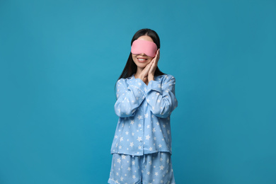 Photo of Young woman wearing pajamas and sleeping mask on blue background. Bedtime