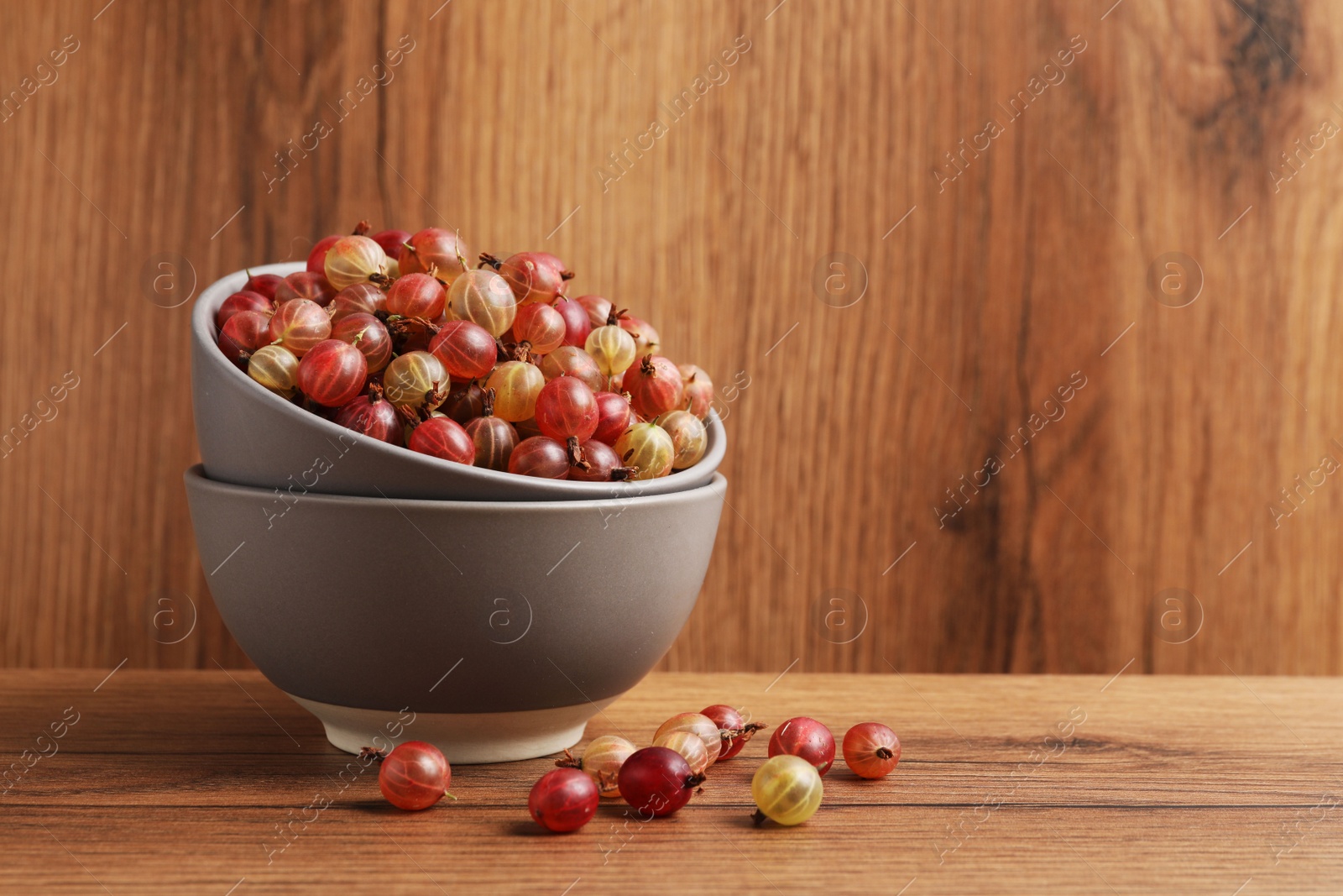 Photo of Bowls full of ripe gooseberries on wooden table, space for text