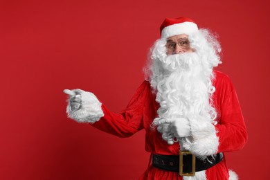 Photo of Merry Christmas. Santa Claus pointing at something on red background, space for text