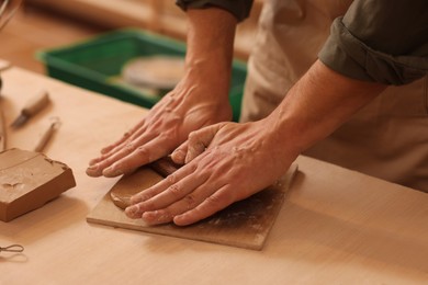 Photo of Man crafting with clay at table indoors, closeup