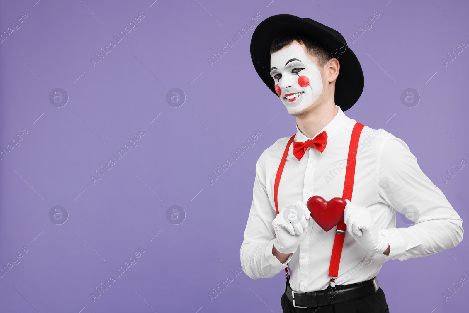 Photo of Funny mime artist with red heart on purple background. Space for text